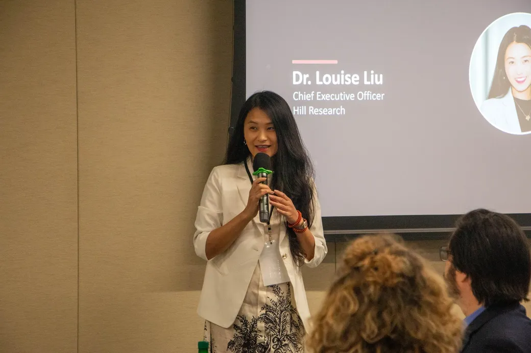Louise Liu speaking with a microphone in front of her title slide.
